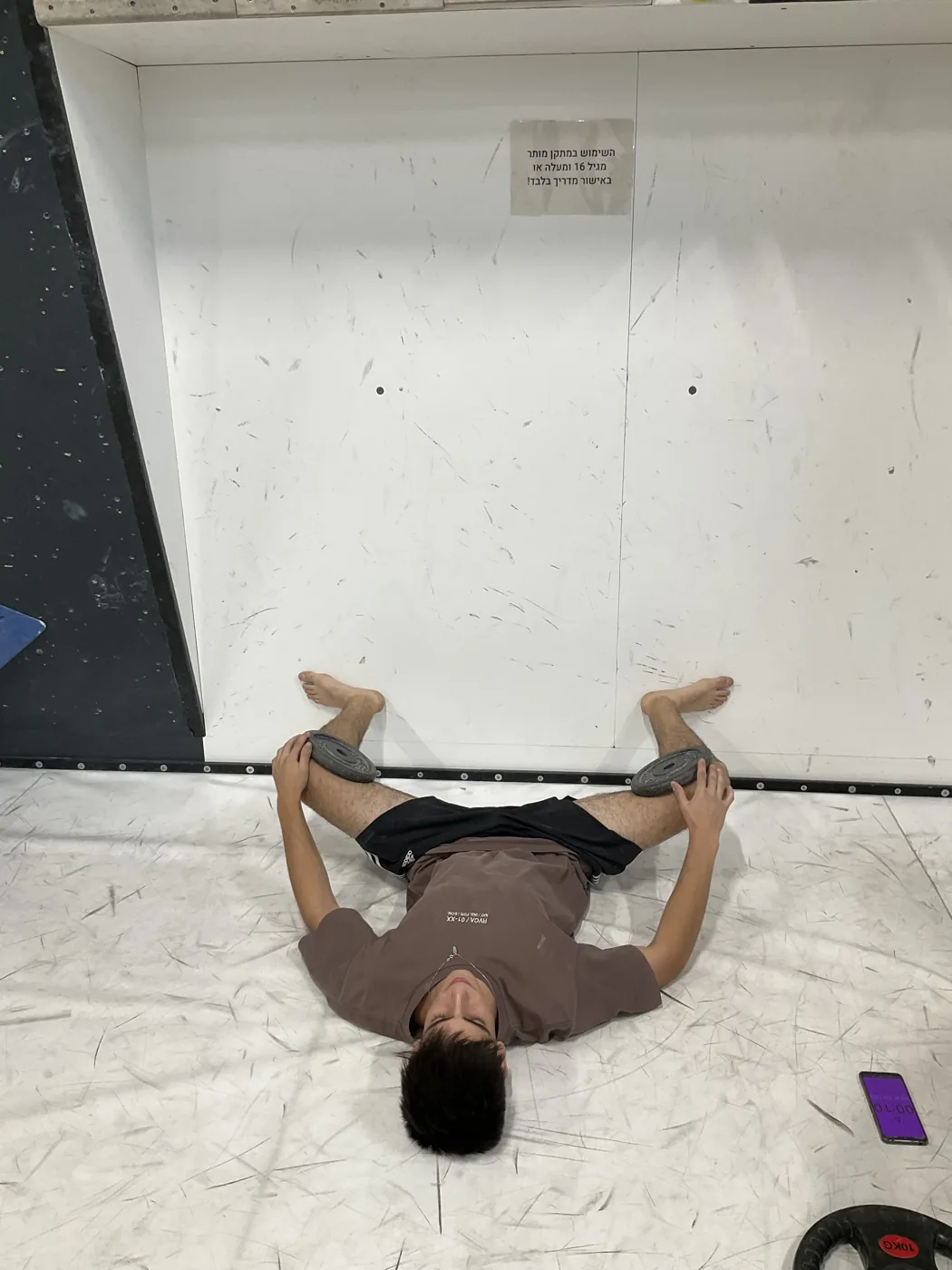 מתאמן מבצע תרגיל מוביליות לפתיחת אגן עם משקולות, בקיר הטיפוס